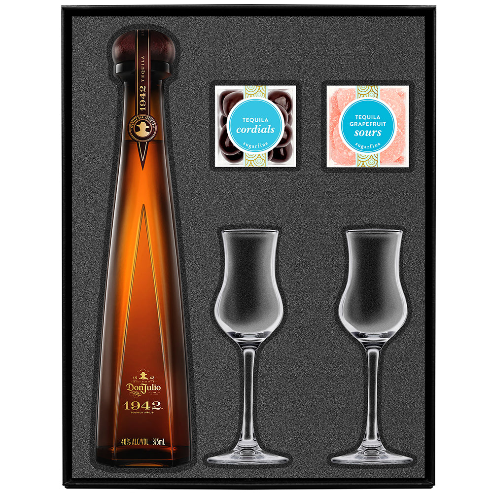 Tequila gift basket with a bottle of Don Julio 1942 tequila, a glass, and snacks on a wooden table outdoors.