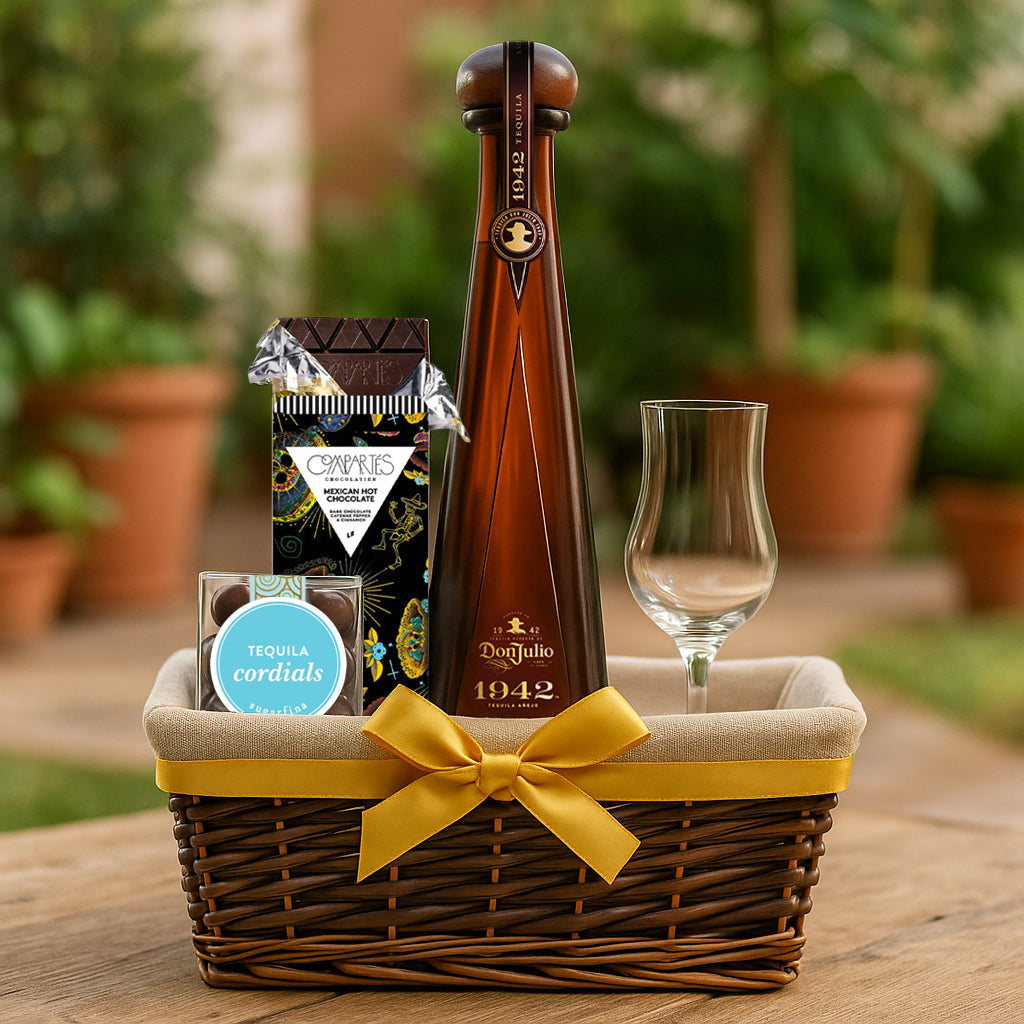 Tequila gift basket with a bottle of Don Julio 1942 tequila, a glass, and snacks on a wooden table outdoors.